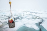 Two researchers are suspended over icy ocean.