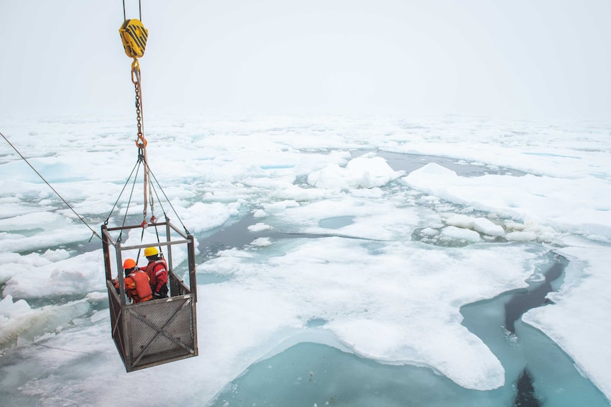 Two researchers are suspended over icy ocean.