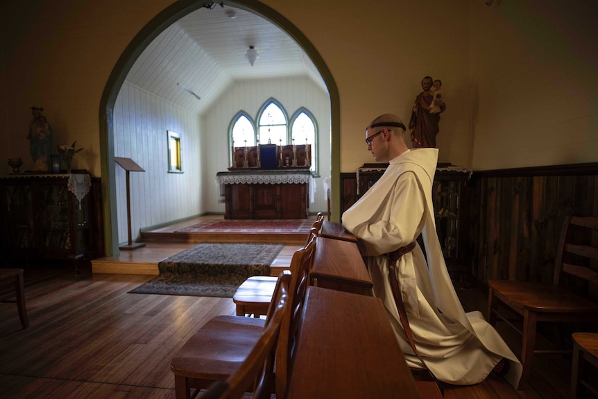 A Benedictine monk in prayer in a small church.