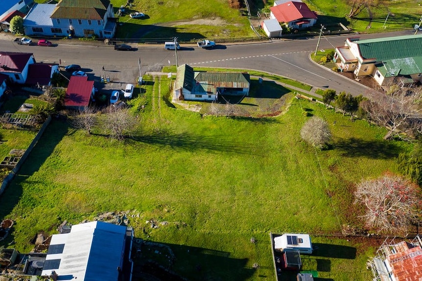 An aerial view of an old house by the roadside with a large expanse of empty land behind it.