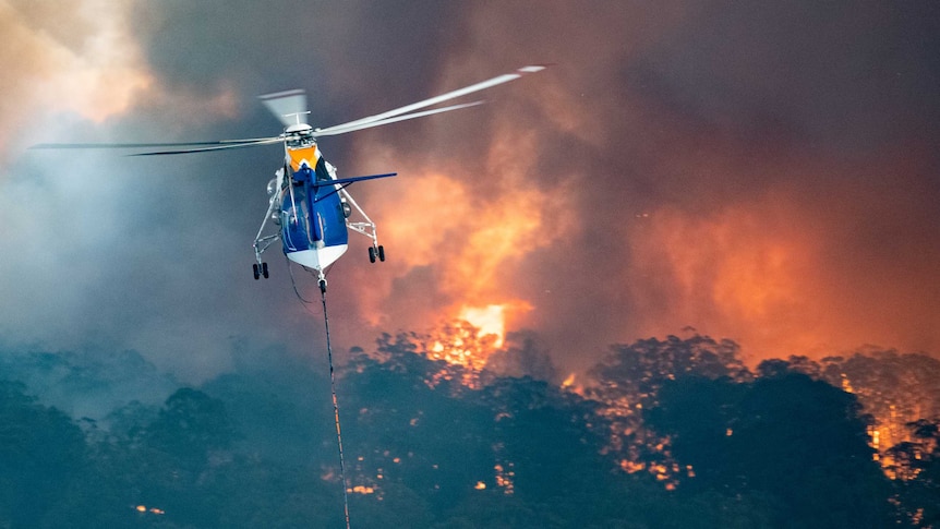 A blue and white helicopter flied above burning bushland.