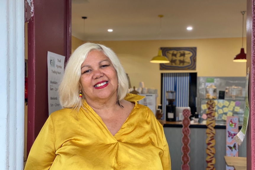 An Indigenous woman smiles at the camera while standing in the doorway of her store