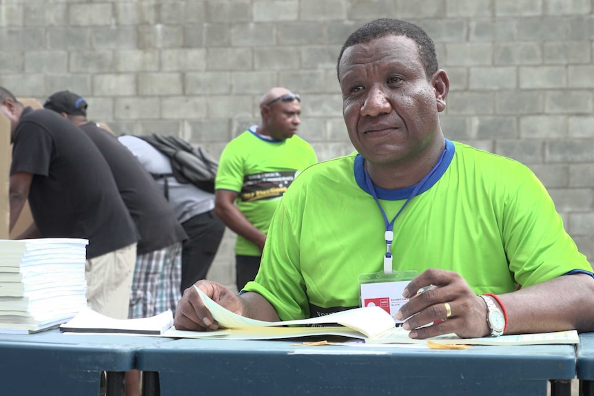 A polling official wearing fluoro yellow signs off on ballot papers at the Tokorara High School, Port Moresby.