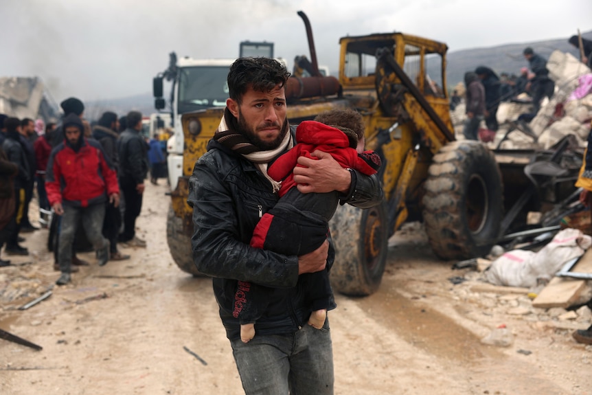 A distressed man carries a baby as he runs along a dusty road in aftermath of earthquake damage