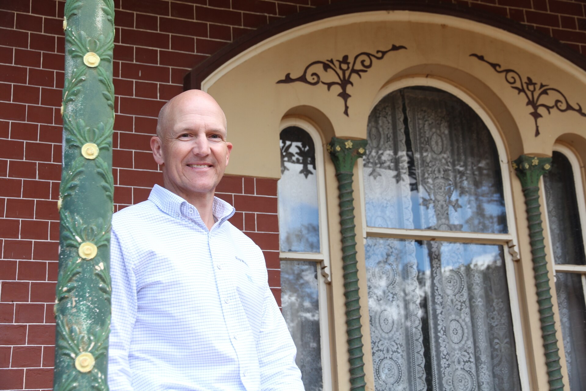 Um homem careca de camisa branca apoiado em um poste. 