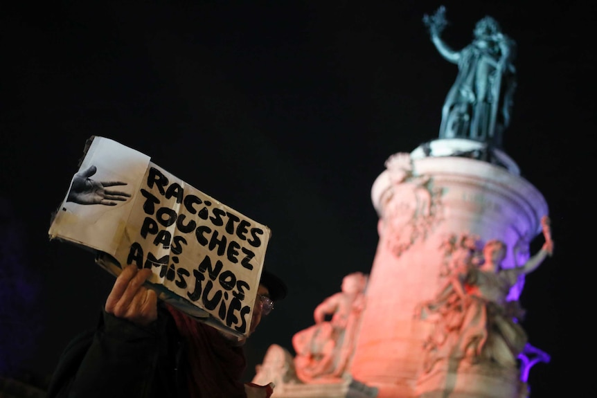 A man holds a poster reading "Racists, Don't Touch to Our Jewish Friends".