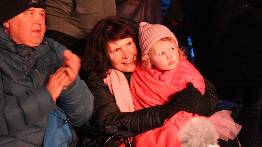 A woman holds a young girl rugged up in pink winter clothing while watching a performance at the Festival of Voices.