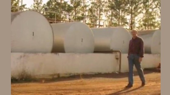 A man stands beside four large tanks