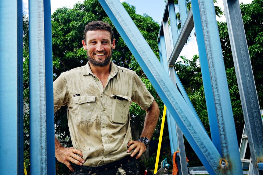 Peter MacFarlane smiles warmly at the camera from a building site where he is behind scaffolding.