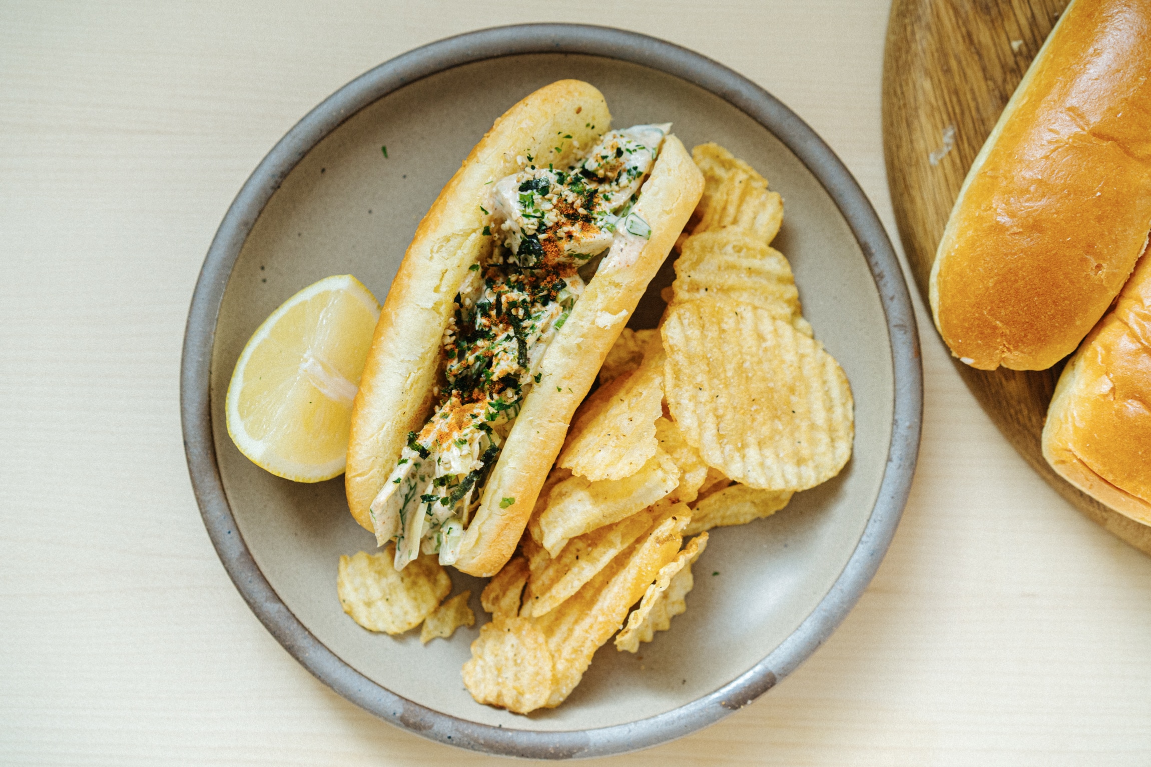 Brioche roll with artichoke, mayonnaise and spice filling, served on a plate with potato chips. 