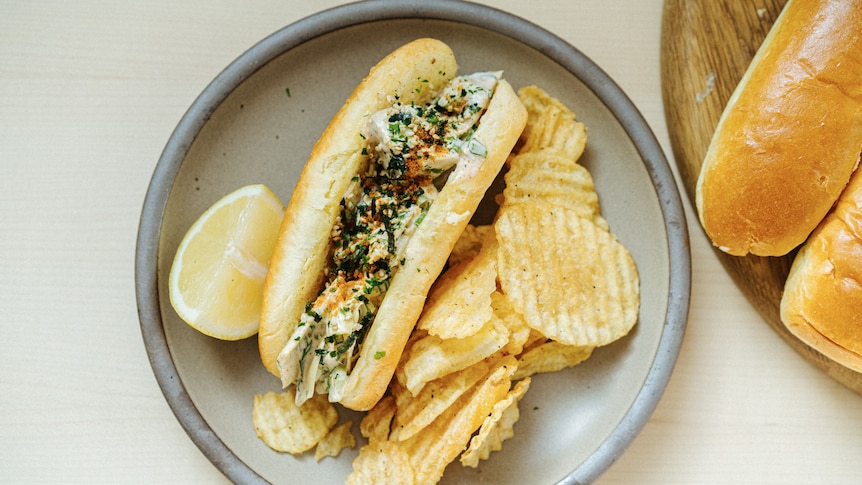 Brioche roll with artichoke, mayonnaise and spice filling, served on a plate with potato chips. 