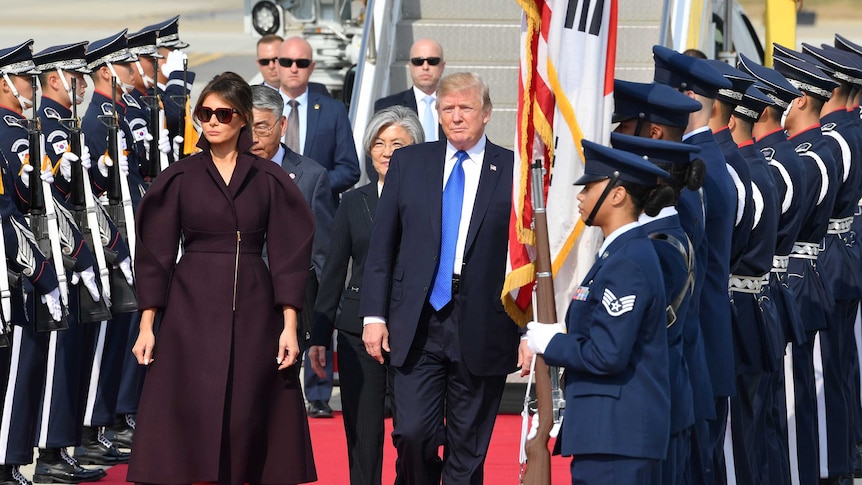 Donald Trump and Melania Trump walk in between two rows of people dressed in military clothing.