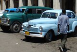 A man walks by a line of cars in the Cuban capital of Havana.