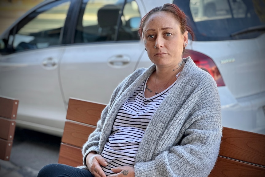 A woman sits on a bench looking unhappy