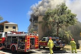 Smoke billowing out of a unit complex in Nedlands, with firefighters in the foreground.