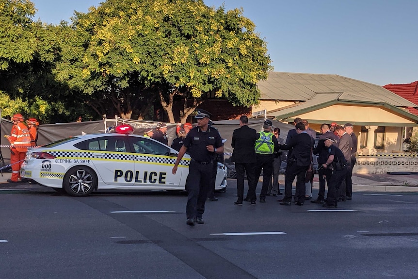 Police officers and a police car on a road in front of a house