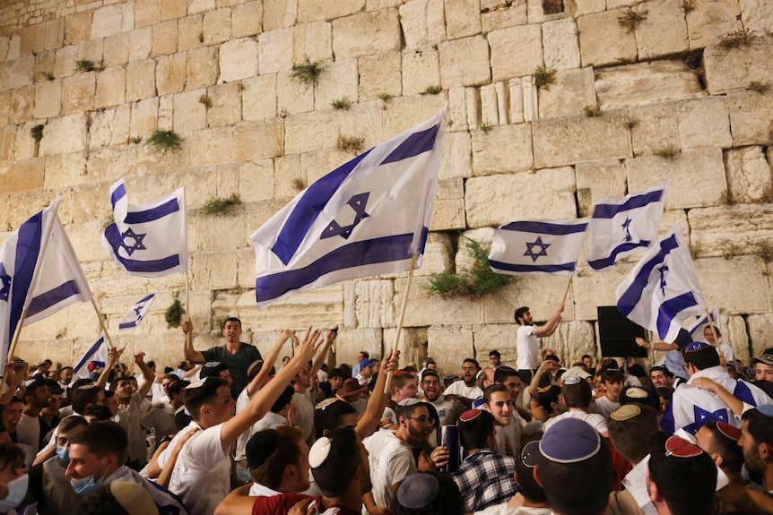 Jewish worshippers dance with Israeli national flags by the Western Wall