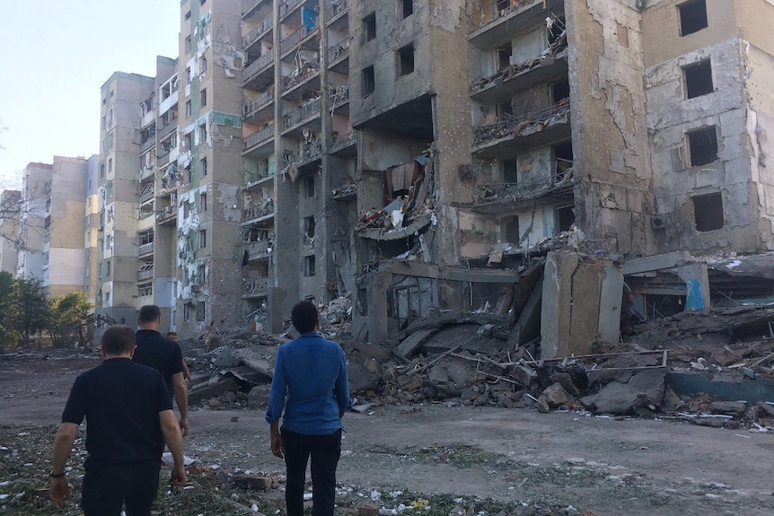 People standig in dirt look up towards a damaged building. 