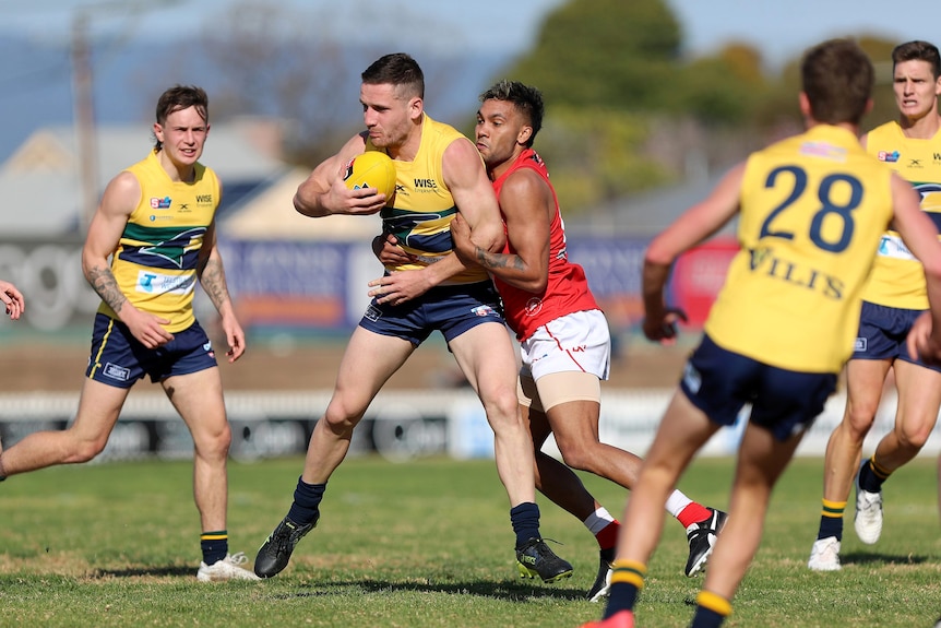 A football player holding the ball is tackled by another player.