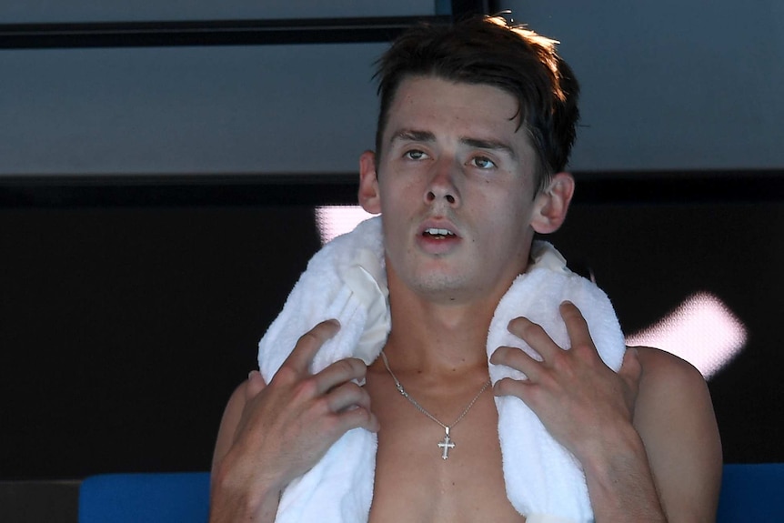 Alex de Minaur with an iced towel around his neck while sitting down during a match at the Australian Open.