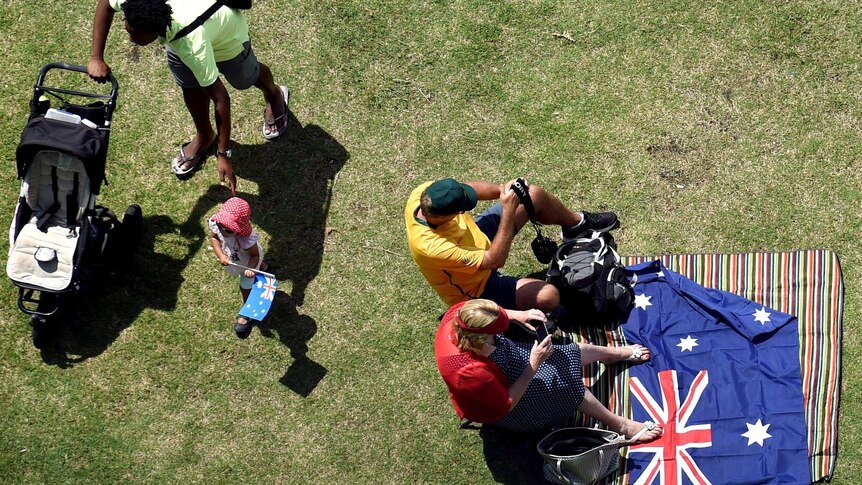 Photo from above of people sitting on a rug on the grass with an Australian flag spread out next to them.