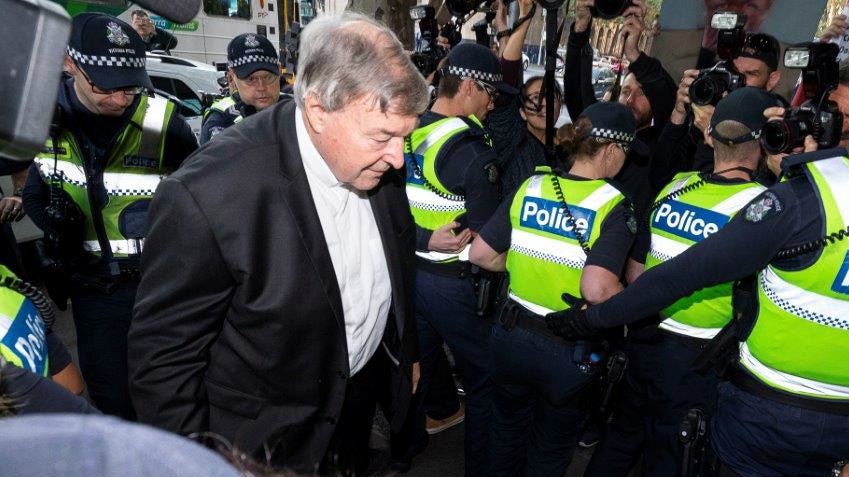 Cardinal George Pell looks down as he walks past a line of police officers as he headed into court.