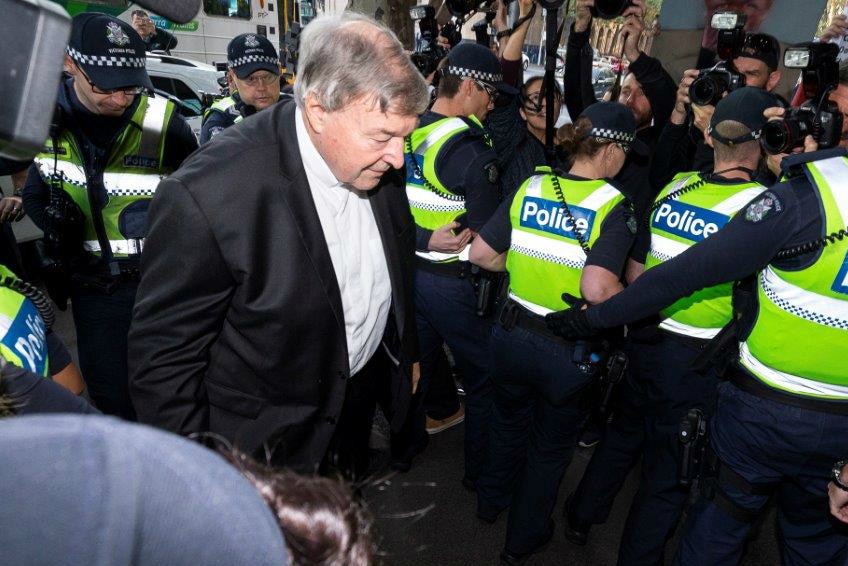 Cardinal George Pell looks down as he walks past a line of police officers as he headed into court.