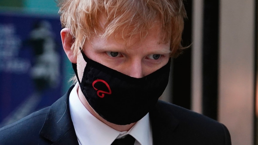 A close up of Ed Sheeran wearing a black face mask 
