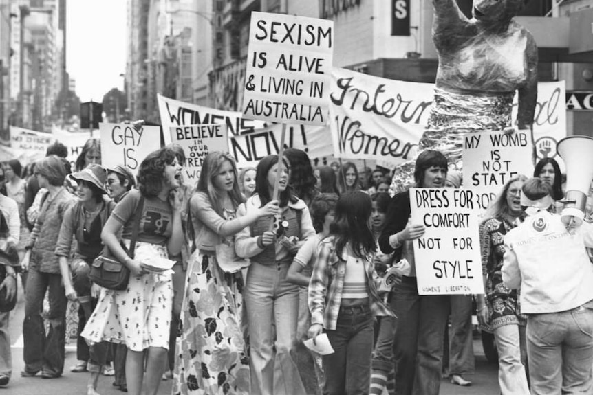 A black and white photo of women marching through the street with placards for the International Women's Day March