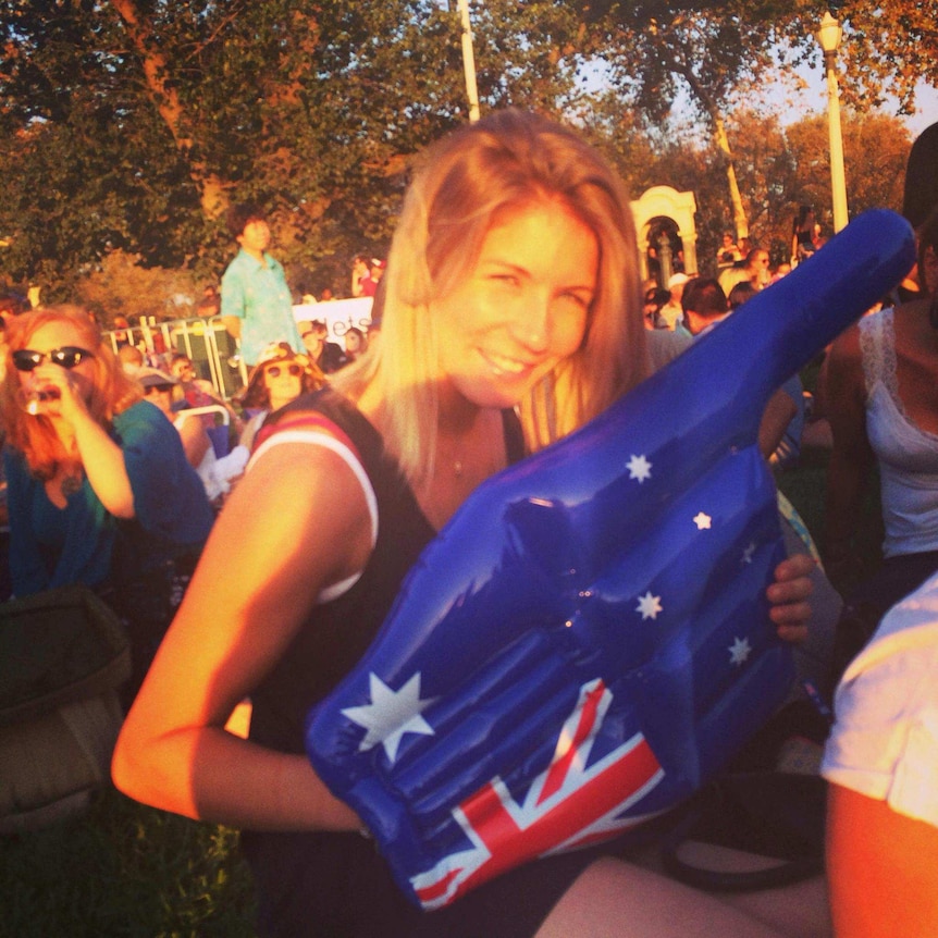 A woman squints into sunlight with a giant inflatable hand on. It has the Australian flag on it.