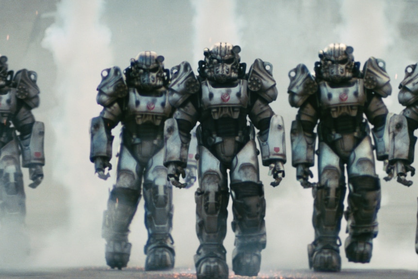 Five people are seen wearing the metal robot suits of the Brotherhood of Steel, as they walk towards the camera.