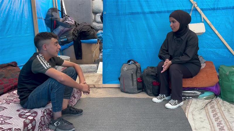 Young woman and man sit under a blue tent