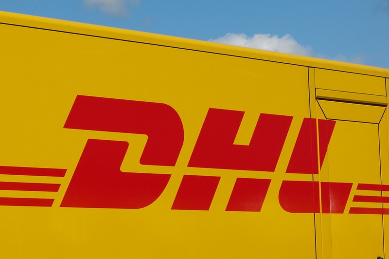 The DHL logo is on a yellow vehicle and there is blue sky and clouds above it
