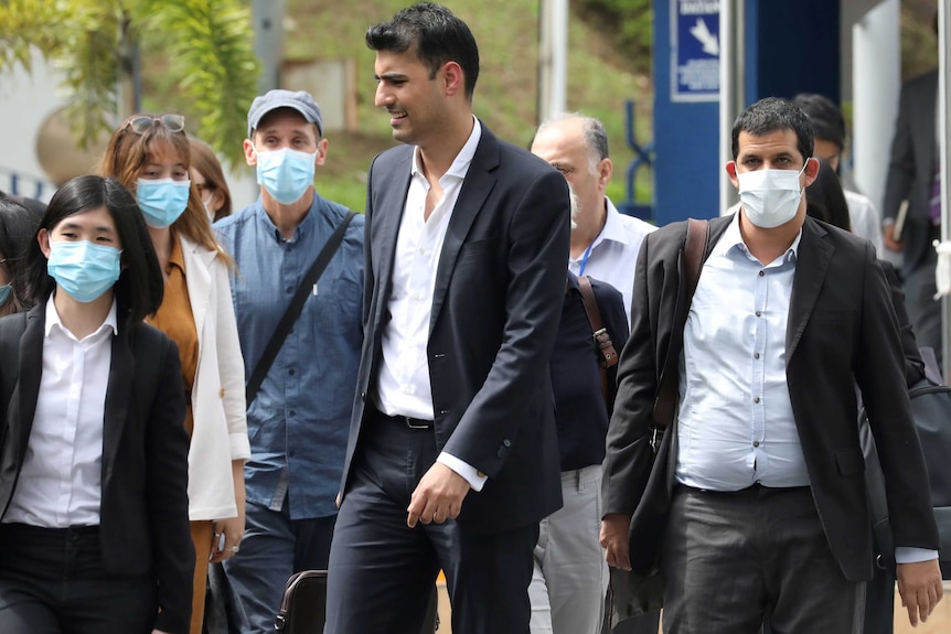 A group of men and women in face masks and suits walk down a street
