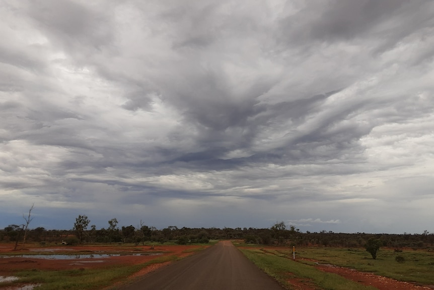 Storms clouds loom over puddles of rain on red dirt