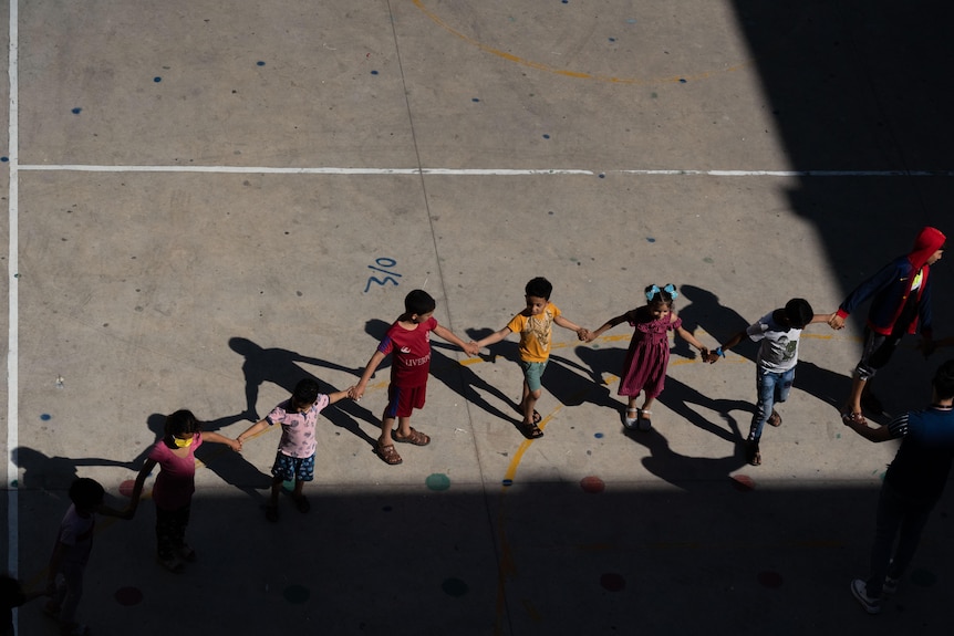 A row of children holding hands in a playground, shot from above