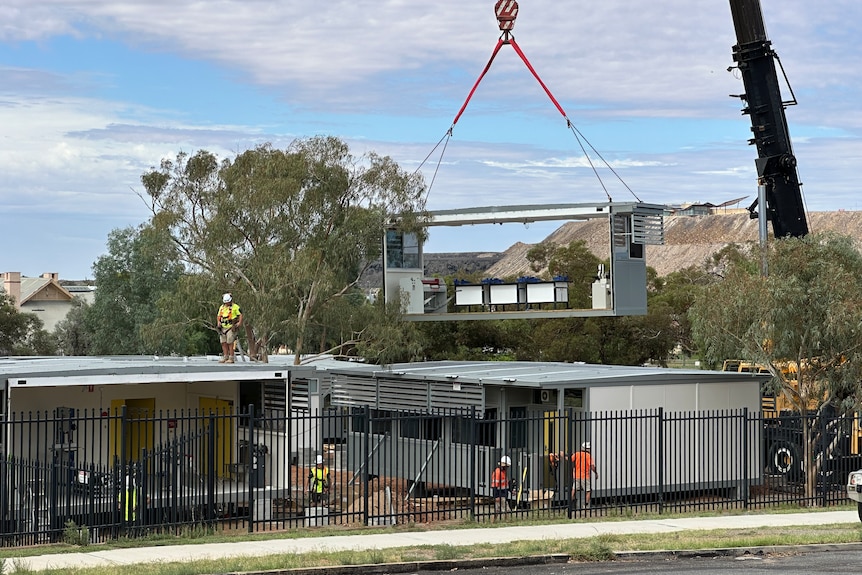 A crane carries a demountable building on to a school oval.