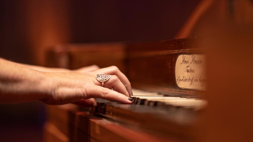 A picture of a woman's hands with a silver ring and black nail polish, playing a heritage piano.