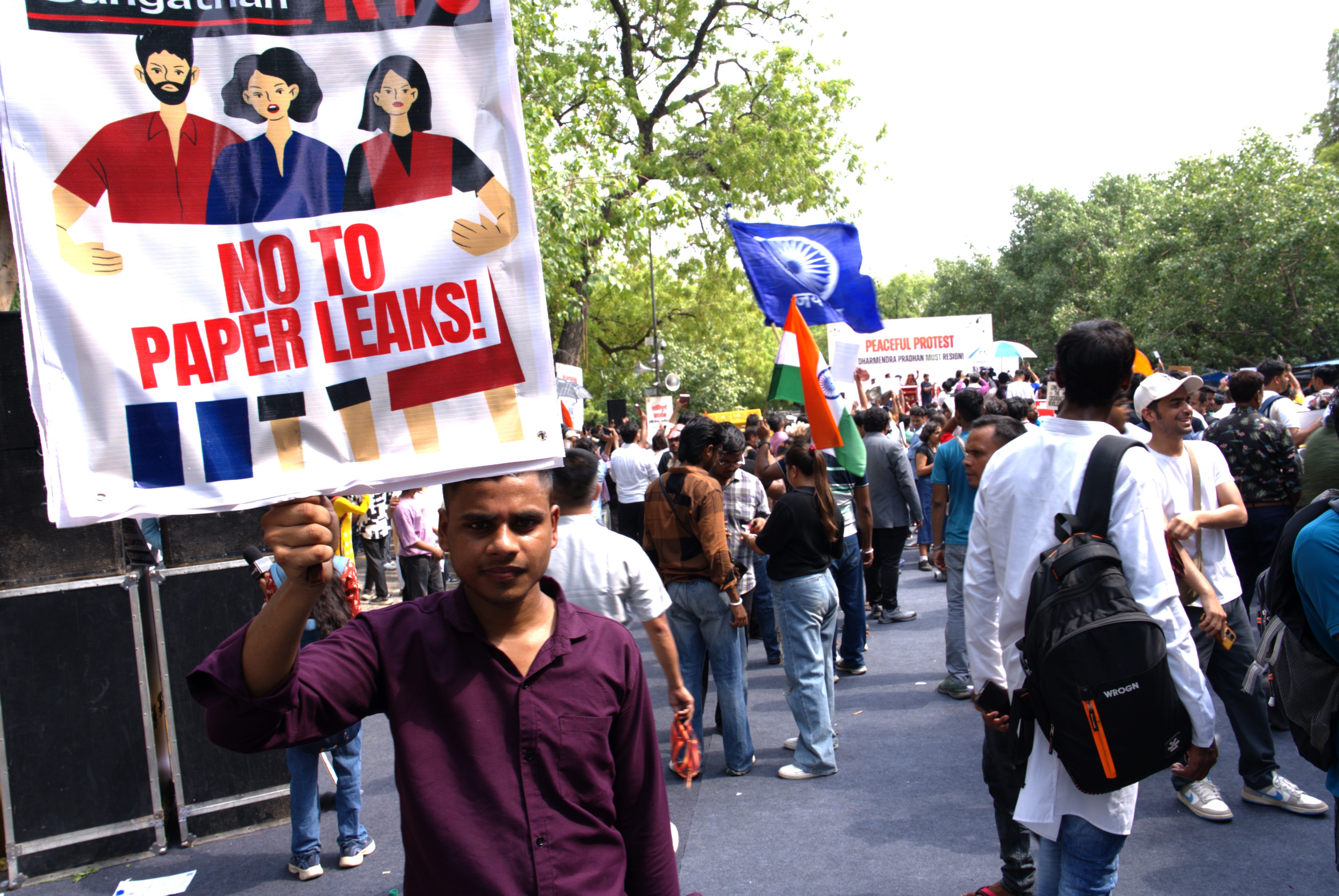 A man with a stern expression holds a sign that says "No to paper leaks" amid a crowd of people near a park.
