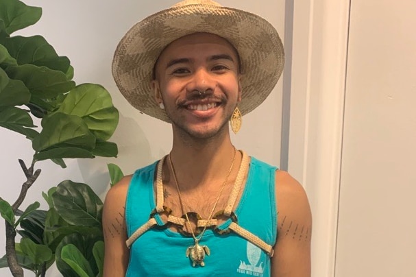 A person wearing a teal singlet with harness across chest and wide-brimmed hat.