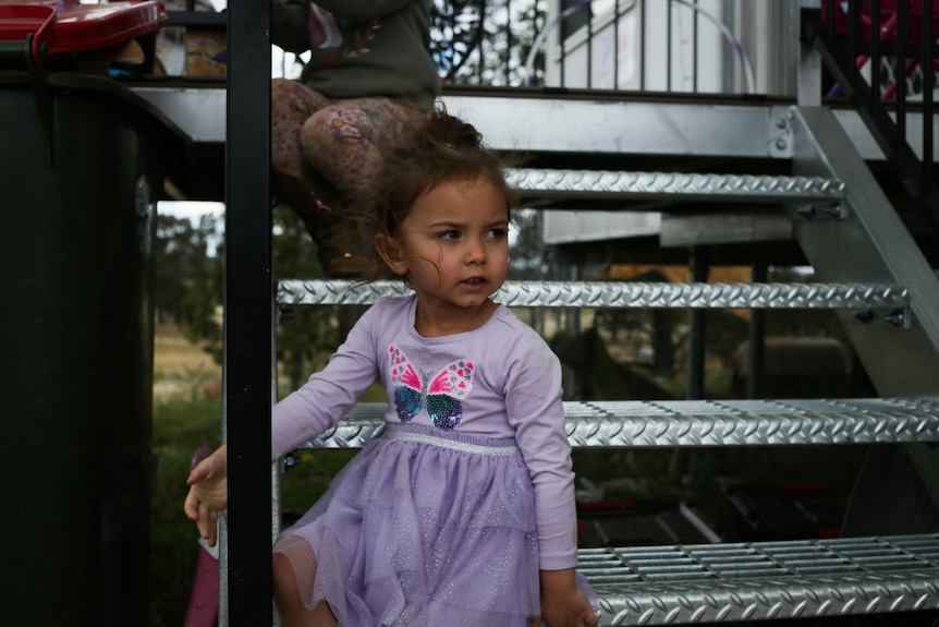 little girl in dress sits on steps of temporary pod home in Eugowra