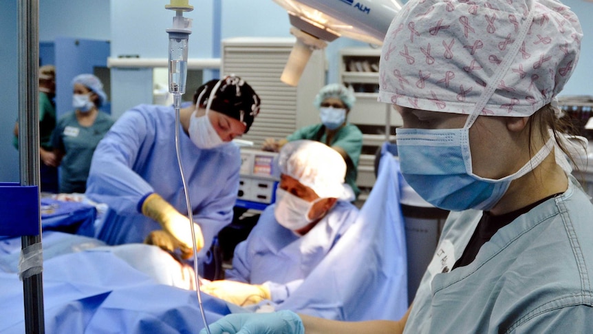 Doctors and nurses in a surgical theatre operate on an unseen patient.