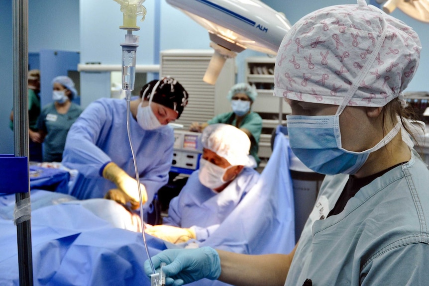 Doctors and nurses in a surgical theatre operate on an unseen patient.