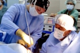 Doctors and nurses in a surgical theatre operate on an unseen patient.