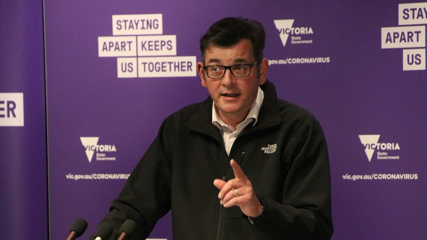 A man stands at a lectern wearing a black jacket.