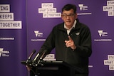 A man stands at a lectern wearing a black jacket.