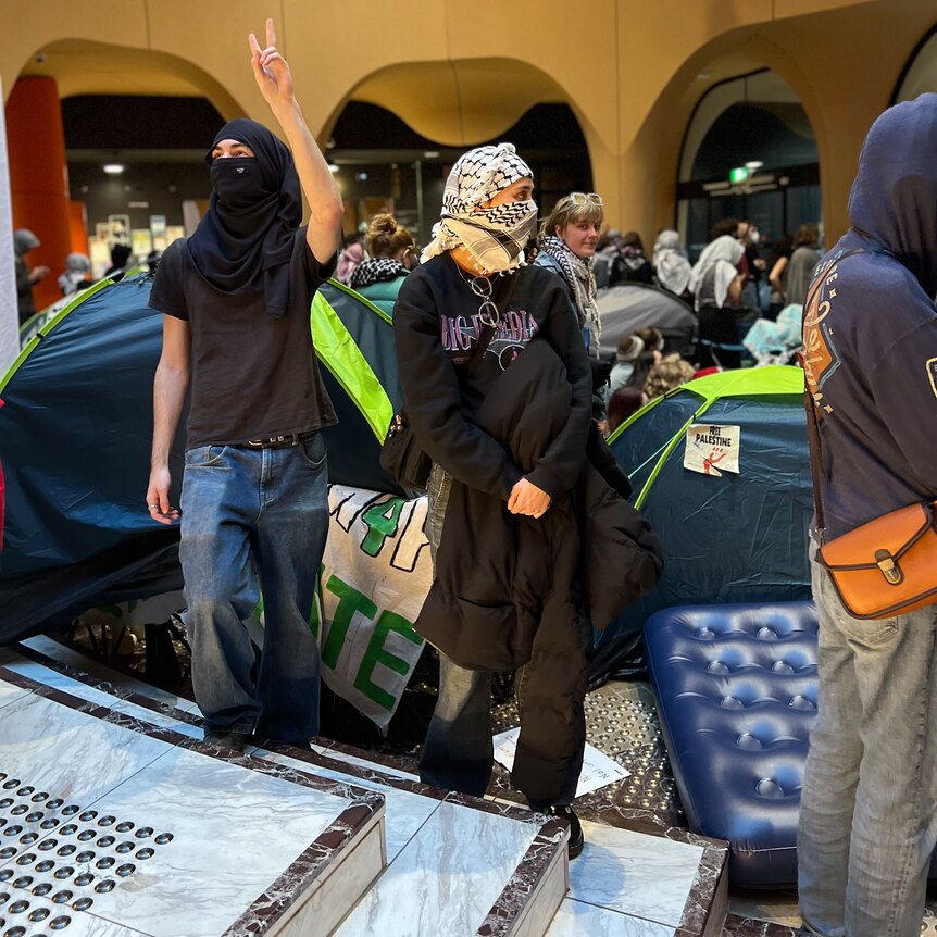 tents set up in a building behind protesters with a mattress on the ground.
