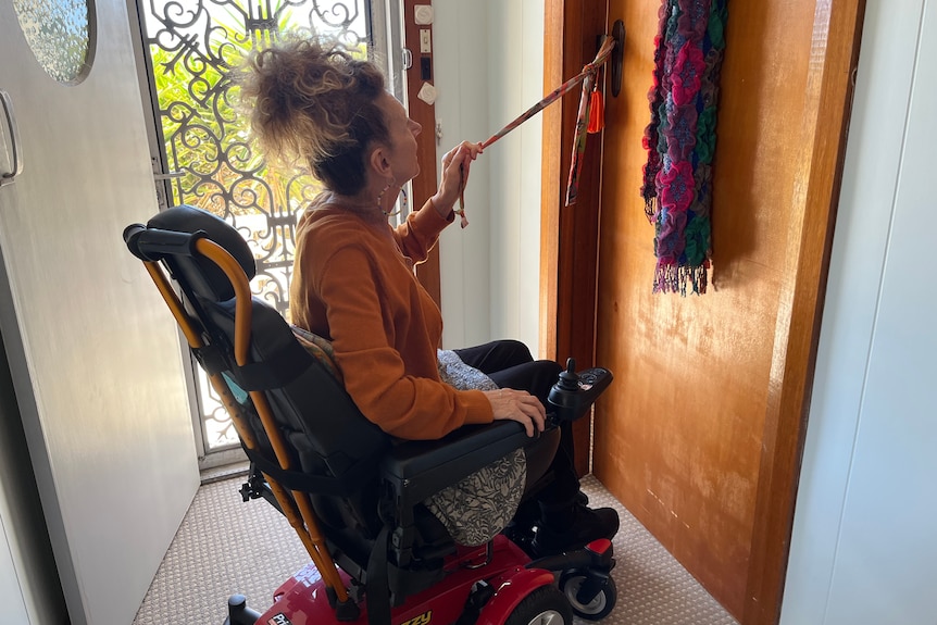 A woman in a wheelchair pulls at a piece of fabric attached to a door handle.