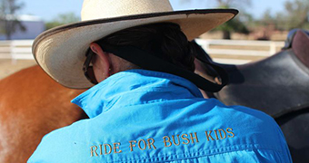 A woman stands by her horse with a "ride for bush kids" shirt on.