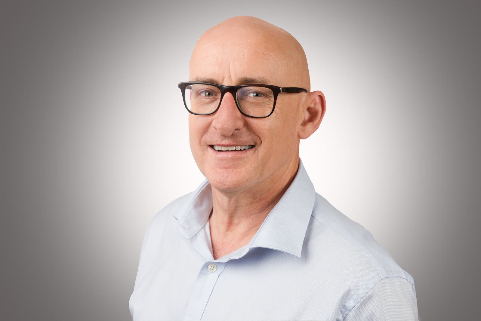 A man wearing black glasses and a blue shirt smiles.
